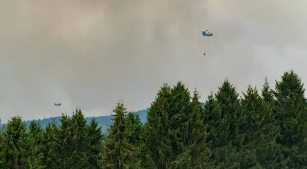 Helikopter bekämpft Waldbrand. Giftiger Rauch steigt auf, der Geruch nach Brand liegt in der Luft.