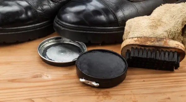 Schwarze Schuhe, Schuhcreme und Bürste auf Holz. So lassen sich Schuhcremeflecken entfernen und die Schuhe pflegen.