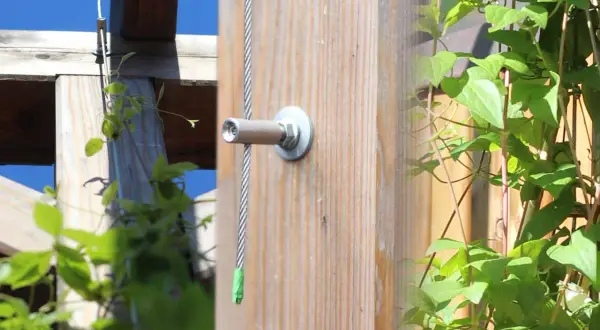 Selbstgebaute Rankhilfe aus Metall: Ein Drahtseil wird an einem Holzpfosten befestigt, um Kletterpflanzen Halt zu geben.