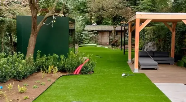 Ein schmal kleinen garten gestalten mit Kunstrasen, Holzpavillon und moderner grüner Wand.