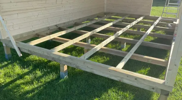 Das Fundament für das Gartenhaus bauen: Holzbalken auf Stelzlagern im Gras, bereit für den Boden.