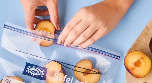 Hände legen halbe Pflaumen in einen Gefrierbeutel. So lassen sich die Früchte perfekt für später einfrieren.