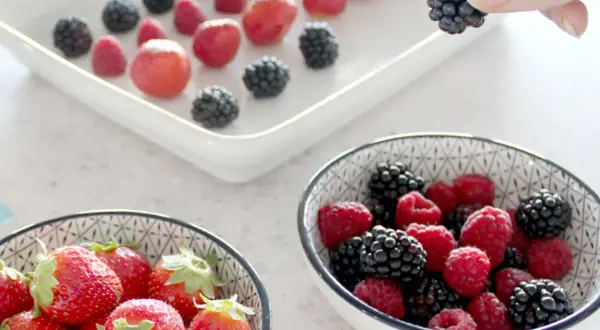 Frische Beeren, darunter Brombeeren, werden für das Einfrieren vorbereitet. Eine Hand hält eine Brombeere.