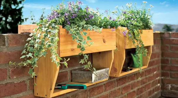 Holz-Blumenkasten selber bauen: Hängende Pflanzen schmücken die Wand. Darunter ein Metallkästchen und eine grüne Gießkanne.