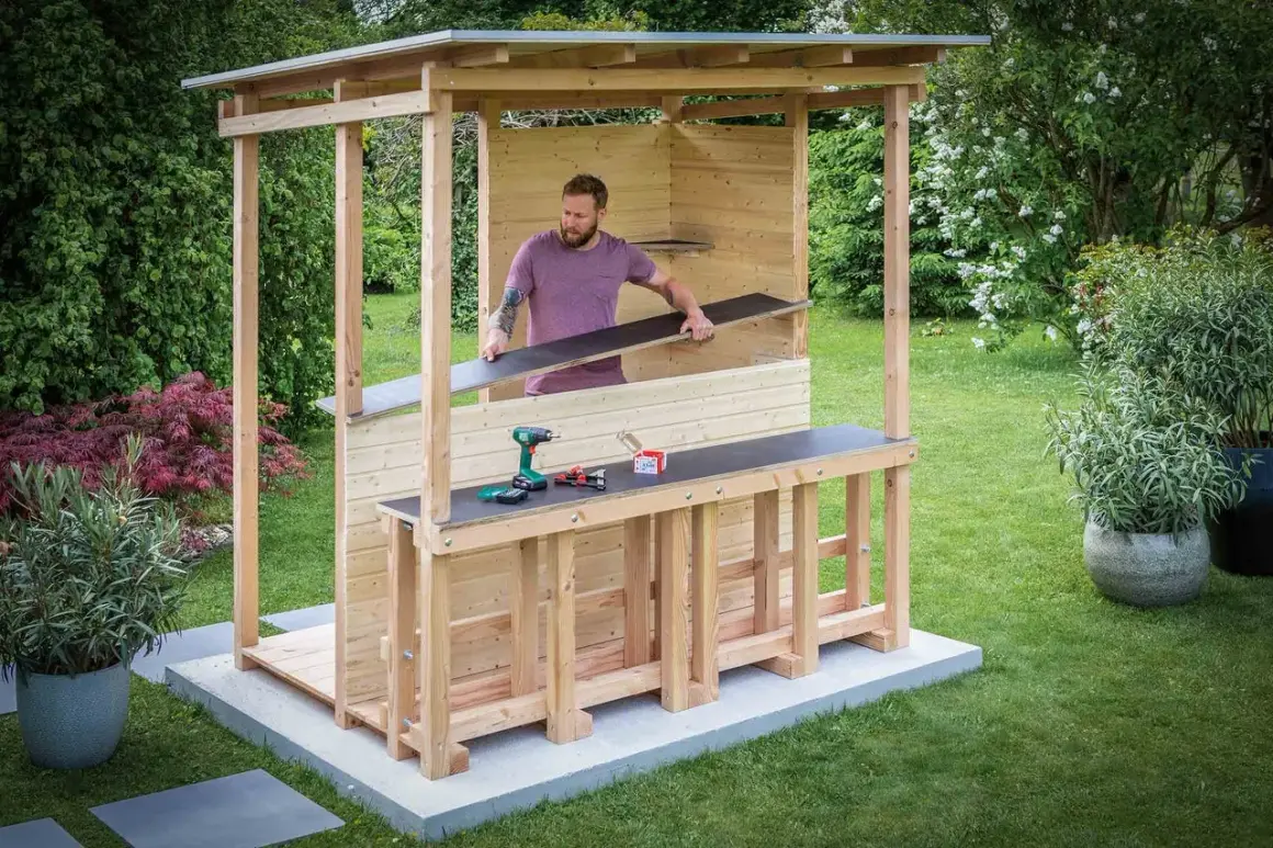 Mann baut eine Gartenbar selber. Holzkonstruktion mit Dach, Tresen und Werkzeug.