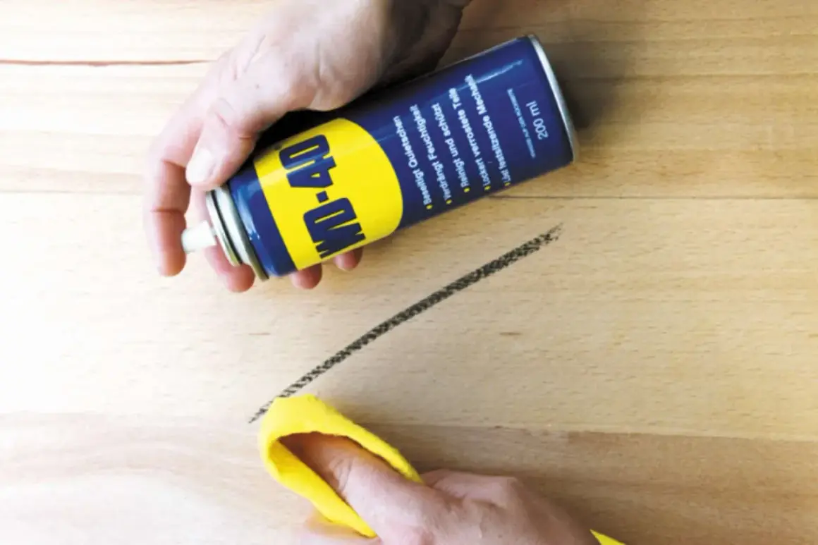 WD-40 Dose sprüht auf einen dunklen Streifen auf hellem Linoleum, der mit einem gelben Tuch abgewischt wird. So lassen sich Streifen auf Linoleum entfernen.