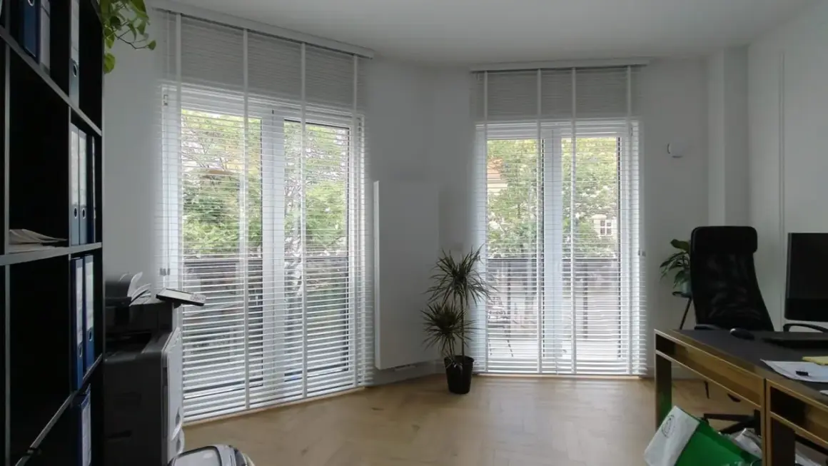 Büro mit vergilbten Plissees reinigen. Helle Räume mit viel Tageslicht, ein Schreibtisch und ein Regal.