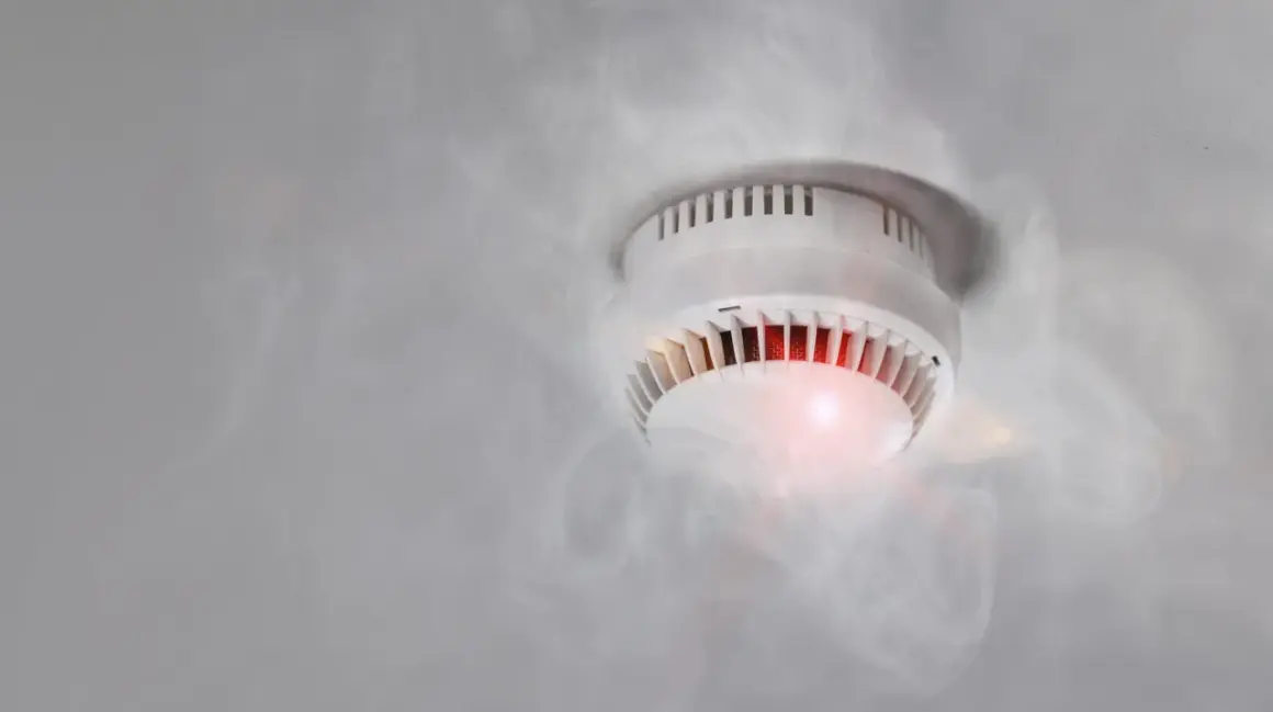 Rauchmelder mit rotem Licht und Dampf, der einen Fehlalarm durch hohe Luftfeuchtigkeit auslöst.