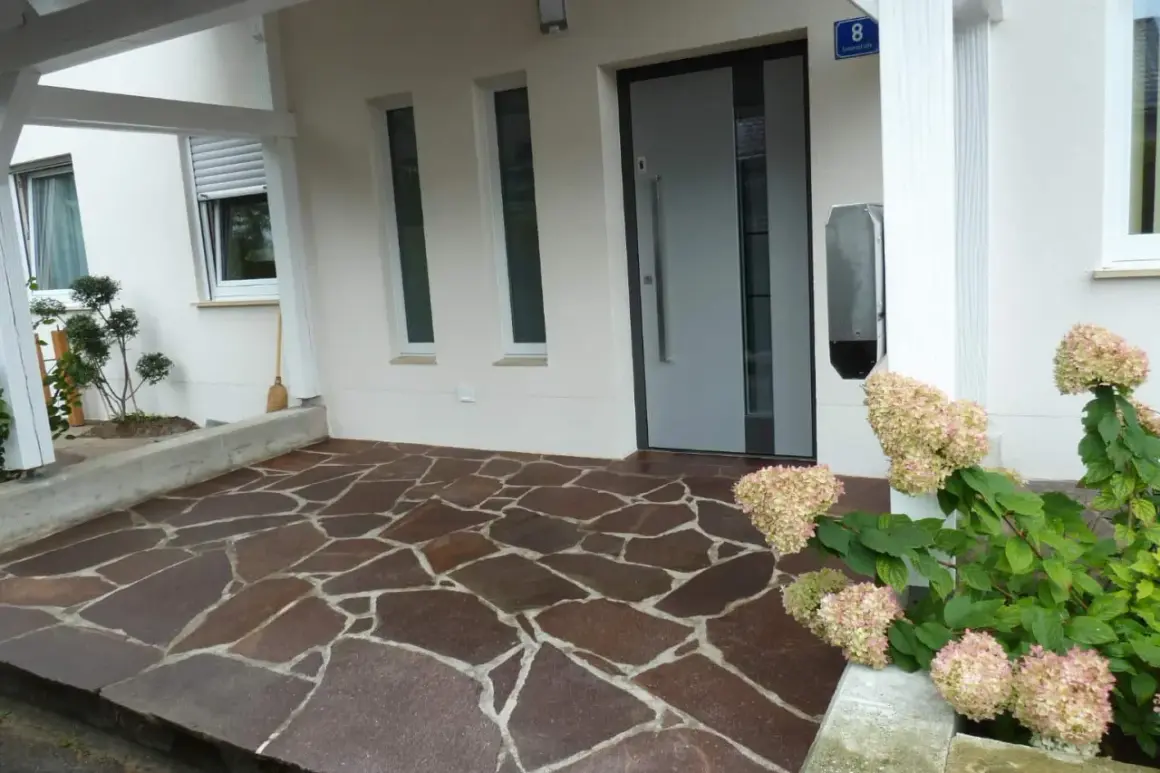 Vor dem Haus liegt ein Boden aus unregelmäßigen Porphyrplatten. Mit Hausmitteln lässt sich dieser Porphyr reinigen und erstrahlt wieder in neuem Glanz.