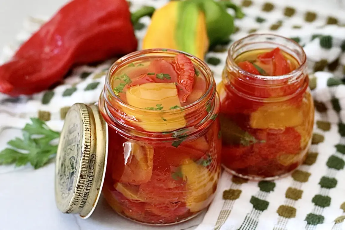 Zwei Gläser mit eingelegter Paprika, daneben frische rote, gelbe und grüne Paprika. Perfekt zum Paprika einkochen.