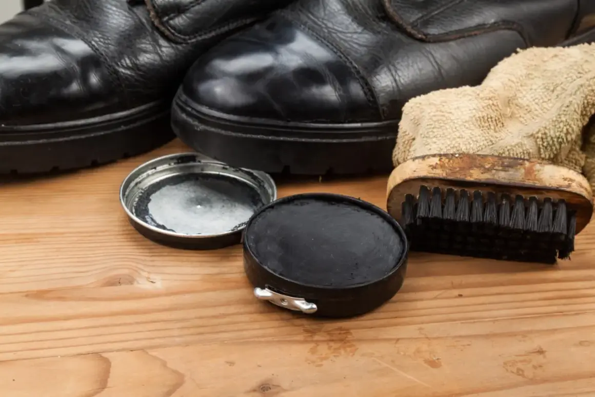 Schwarze Schuhe, Schuhcreme und Bürste auf Holz. So lassen sich Schuhcremeflecken entfernen und die Schuhe pflegen.