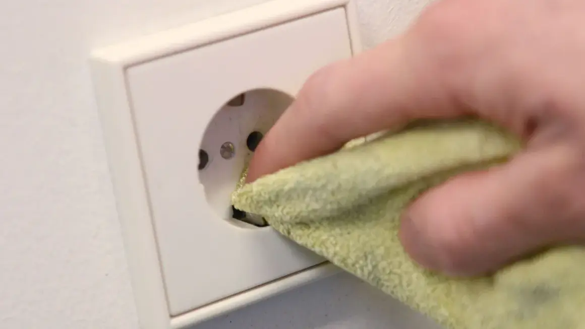 Finger mit Tuch reinigt Steckdose, um sie sicher und sauber zu halten. Steckdosen reinigen ohne abschrauben ist so einfach.