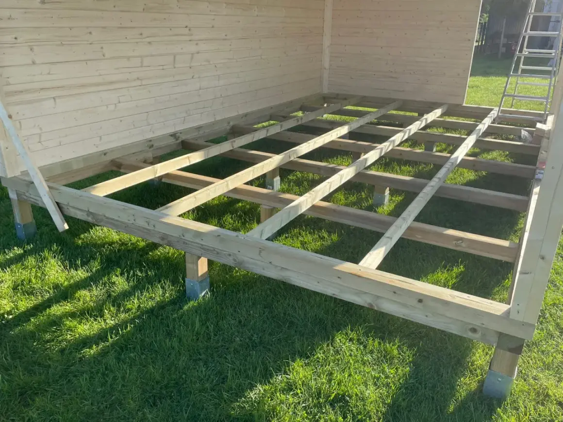 Das Fundament für das Gartenhaus bauen: Holzbalken auf Stelzlagern im Gras, bereit für den Boden.