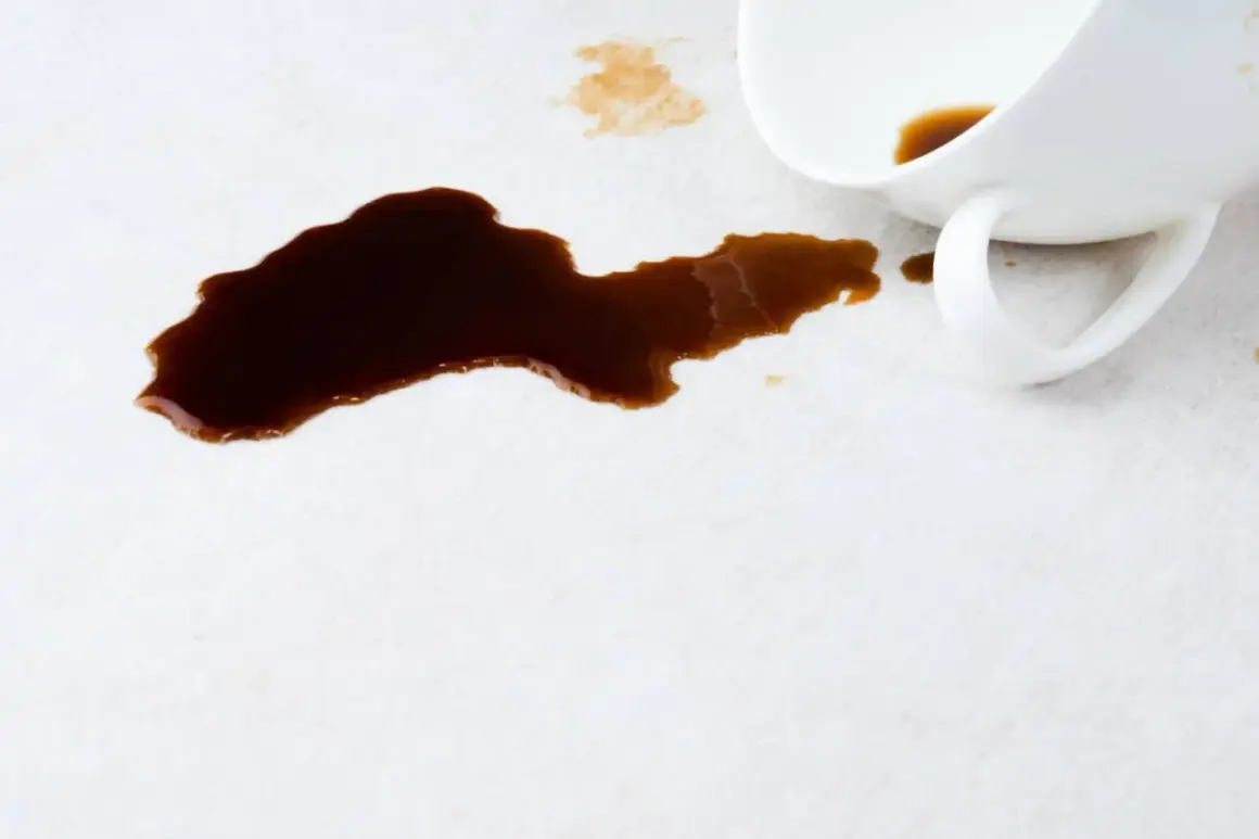 Ein umgekippter Becher hat dunklen Kaffee auf einen hellen Teppich verschüttet. So kann man Kaffee aus Teppich entfernen.