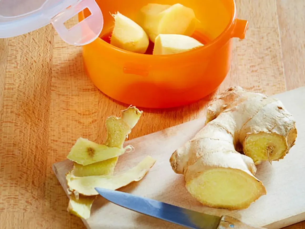 Frisch geschältes Ingwerstück liegt neben einem Messer auf einem Holzbrett. Ein orangefarbener Behälter mit weiteren Ingwerstücken ist bereit zum **ingwer einfrieren**.