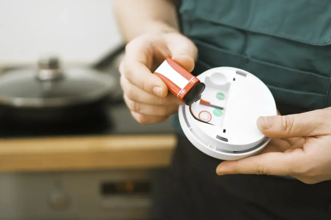 Hände tauschen eine Batterie in einem Rauchmelder aus. Sicherheit geht vor, darum den Rauchmelder regelmäßig warten.