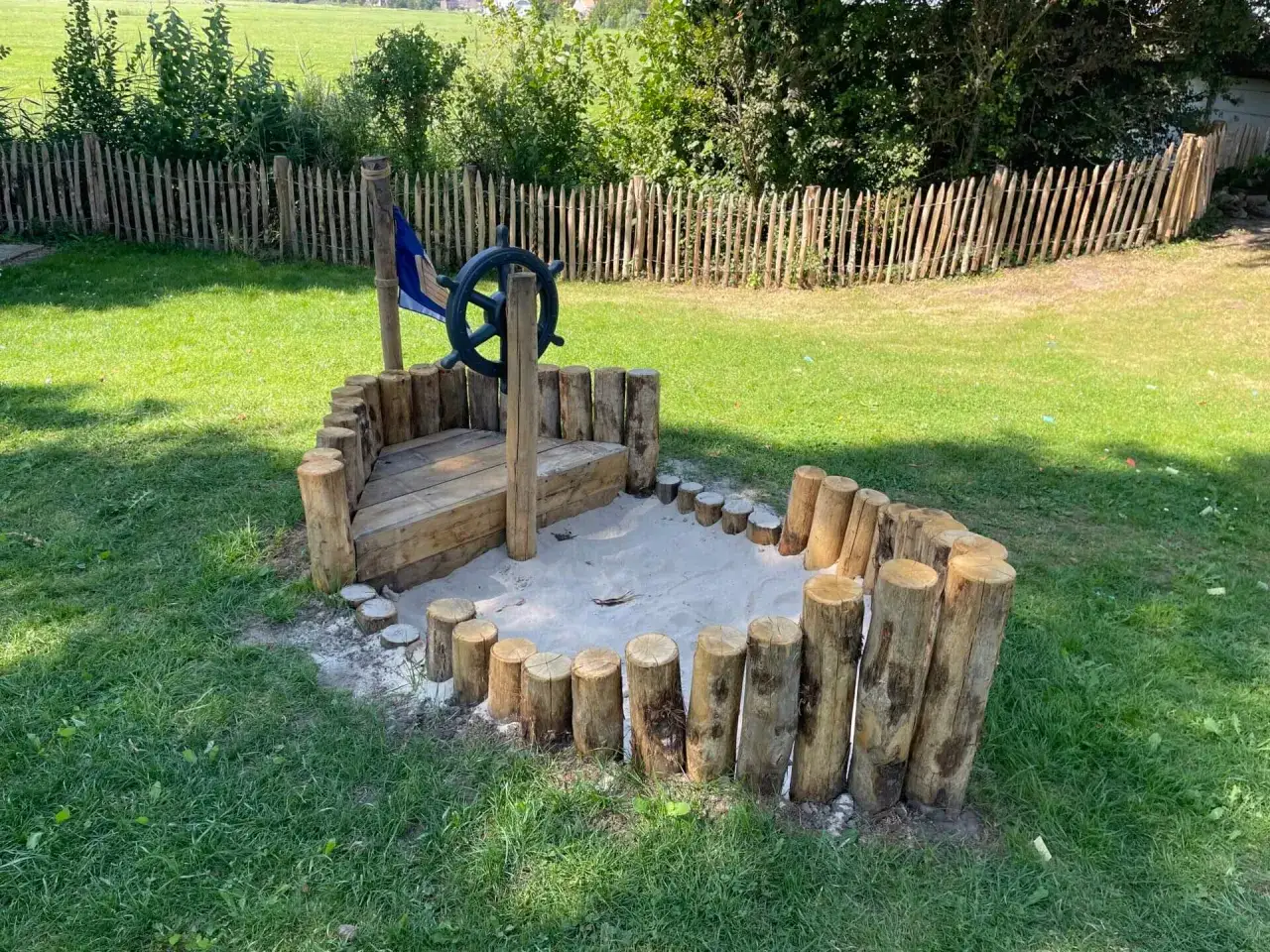 Ein selbstgebauter Sandkasten in Schiffsform mit Steuerrad und Flagge. Perfekt f&uuml;r kleine Seefahrer!