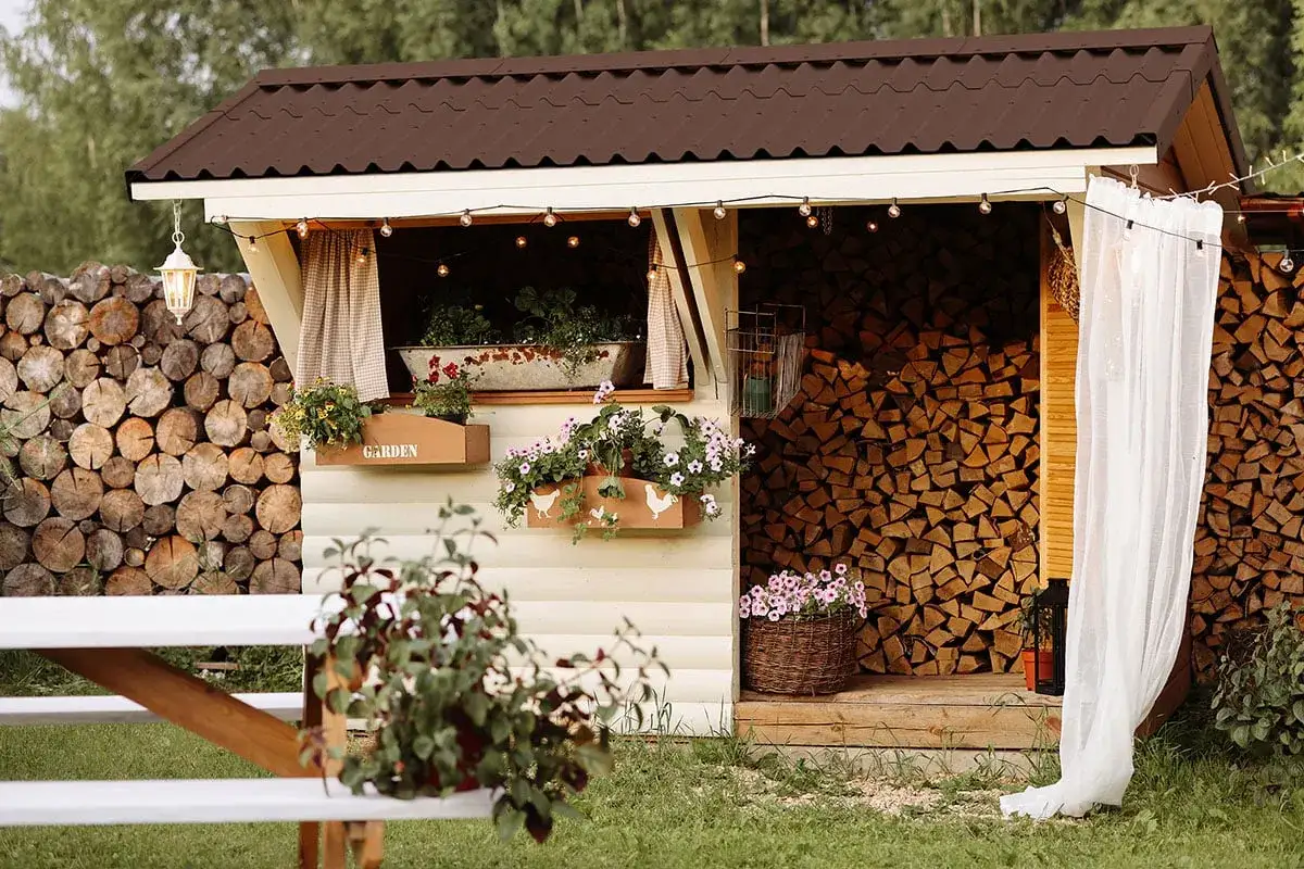 Ein gem&uuml;tlicher Holzunterstand, gebaut mit Liebe zum Detail. Mit Blumenk&auml;sten, Lichterketten und einem Korb voller Bl&uuml;ten.