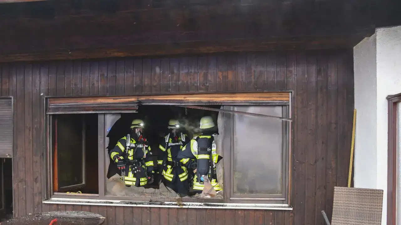 Feuerwehrleute untersuchen ein Fenster, durch das Rauch dringt. Was tun, wenn die steckdose brennt? Sofort Strom abschalten!