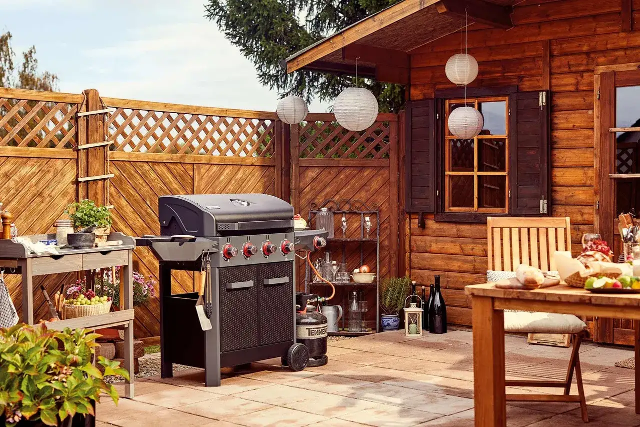 Gemütliche Gartenecke mit Grill, Holzhütte und Tisch. Perfekt, um einen Grillunterstand selber bauen zu lassen und den Sommer zu genießen.