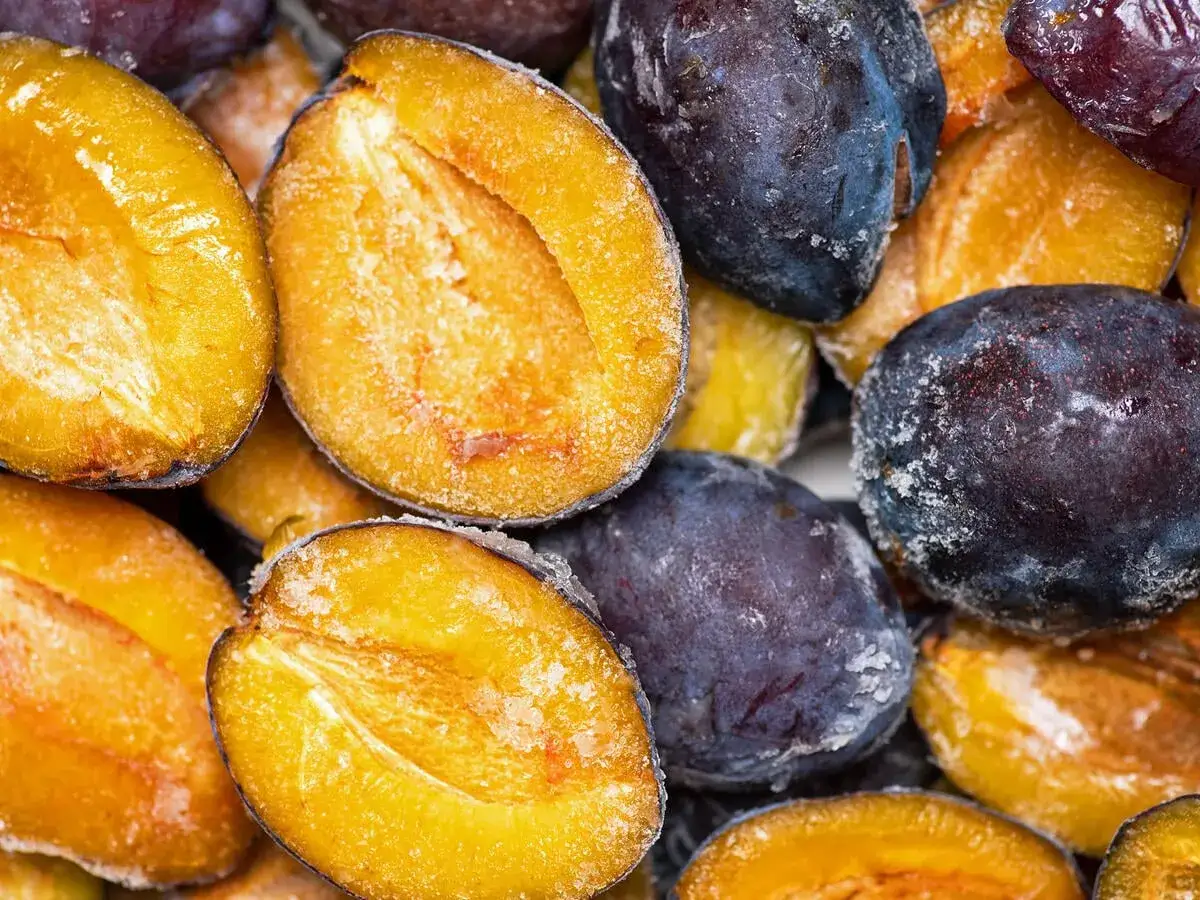 Gefrorene Pflaumen, einige halbiert, zeigen ihr saftiges Fruchtfleisch. Perfekt für pflaumen einfrieren.
