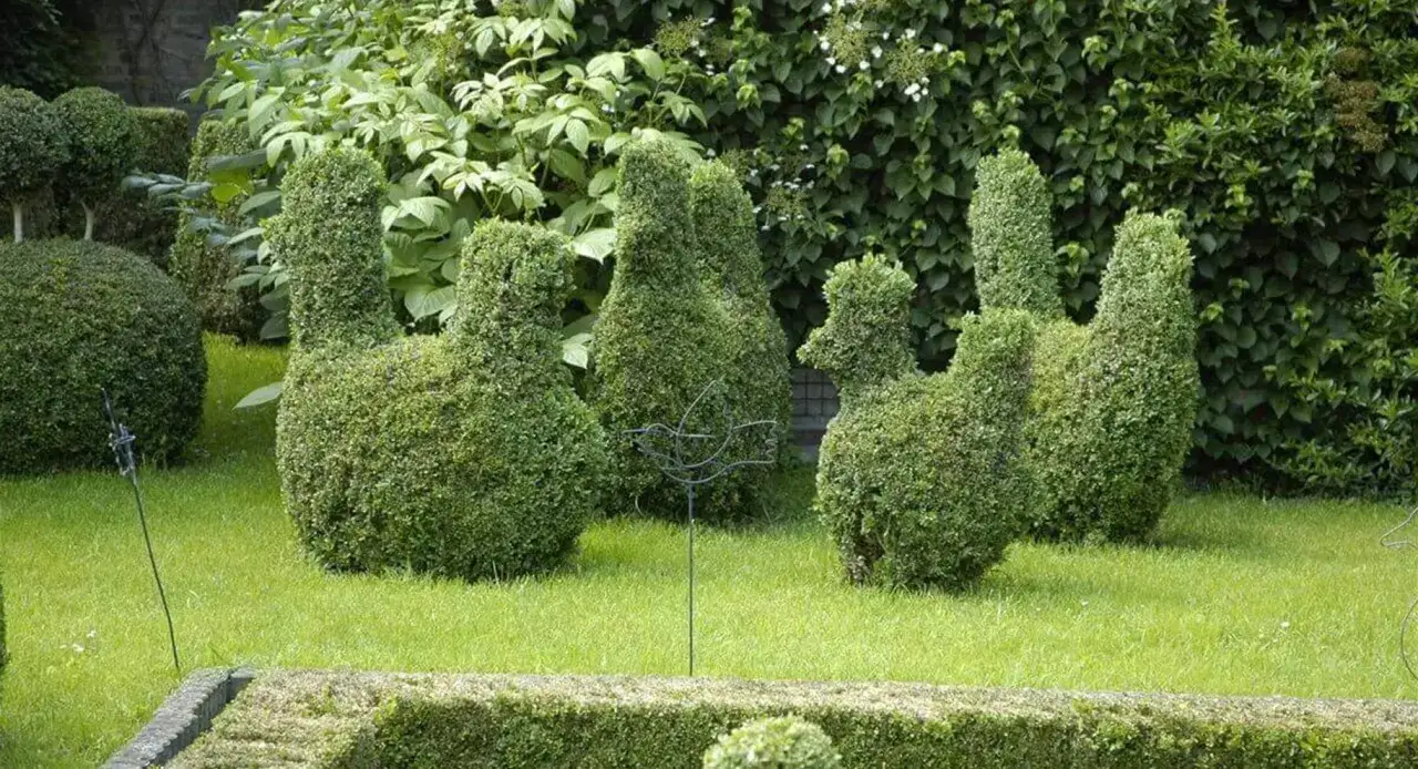 Gr&uuml;ne Tierfiguren aus Buchsbaum, kunstvoll geschnitten, stehen im Garten. Eine Eibe schneiden ist hier eine Kunst.