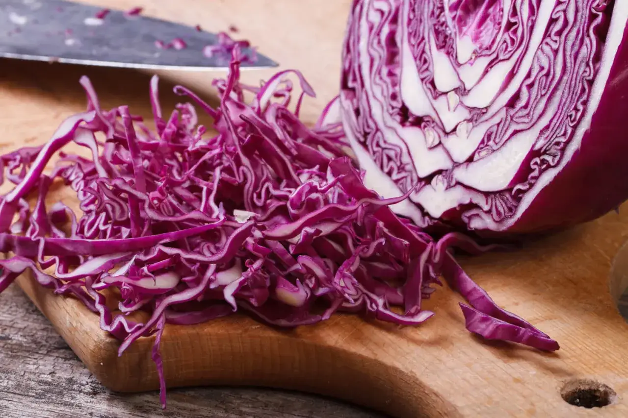 Ein halber Rotkohl und fein geschnittene Streifen liegen auf einem Holzbrett. Perfekt vorbereitet f&uuml;r das Rotkohl einfrieren.