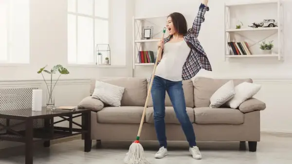 Frau singt und tanzt mit einem Mopp, während sie ihr Linoleum mit Hausmitteln reinigt.