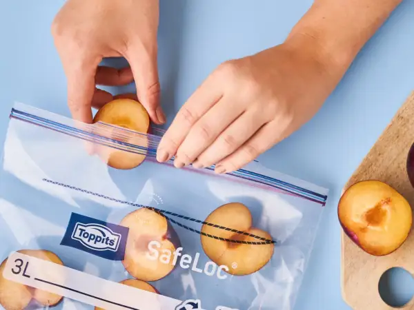 Hände legen halbe Pflaumen in einen Gefrierbeutel. So lassen sich die Früchte perfekt für später einfrieren.