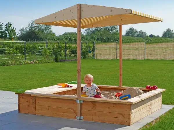 Ein Kind spielt im **Sandkasten selber bauen**. Der Holzsandkasten mit Sonnendach steht im Garten.
