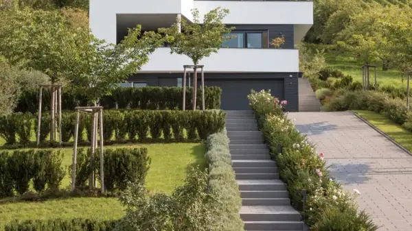 Moderner Garten am Hang mit gepflasterter Auffahrt, Treppen und üppiger Bepflanzung.