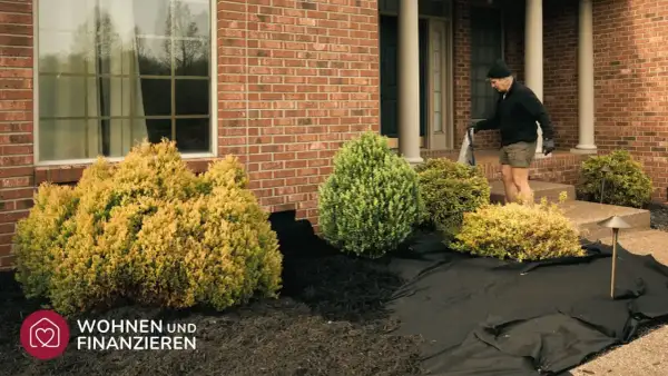 Mann legt Vlies aus, um den Vorgarten zu gestalten. Neue Pflanzen und Mulch werden vorbereitet.